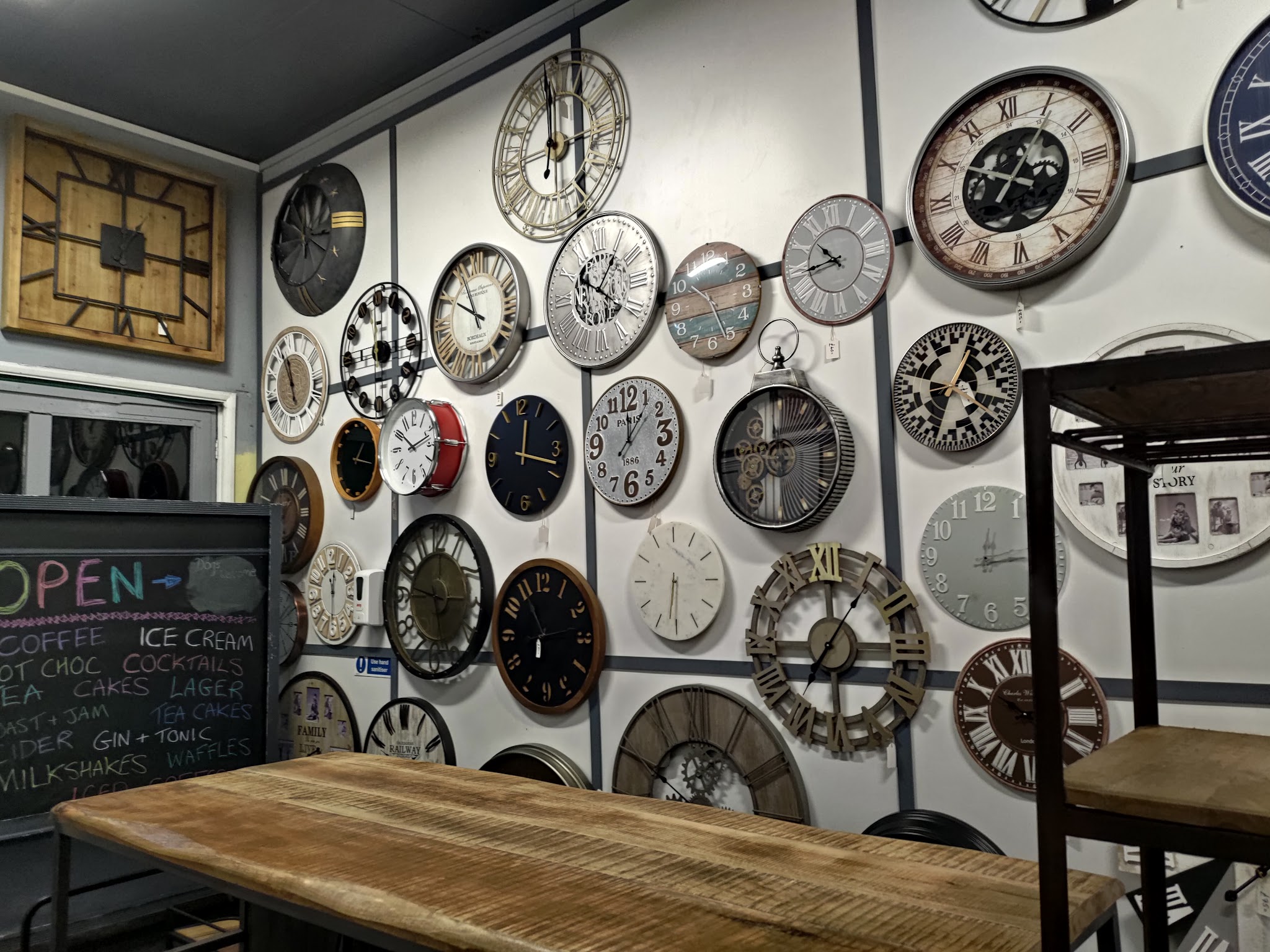 The coffee shop chalkboard menu beside a wall of clocks and a long wooden table