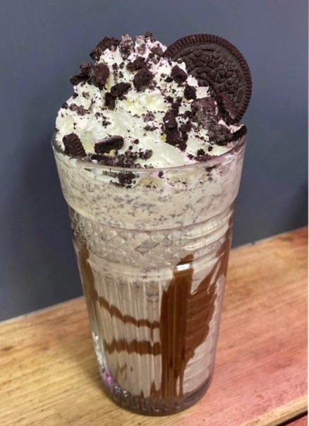 A tall cookies and cream milkshake topped with cream and a biscuit